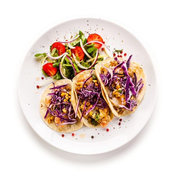 Three tacos filled with shrimp, corn, and purple cabbage, served with a side salad.